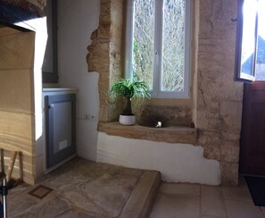 A rustic room with a stone wall, a window with white shutters, a potted plant, and a small metal basin. - Cottage of charm and character, 220 m2, quiet, between Sarlat and Lascaux. (Archignac)