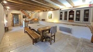 A rustic interior with exposed wooden beams, a stone fireplace, a dining area with benches, and a staircase leading to an upper level. - Cottage of charm and character, 220 m2, quiet, between Sarlat and Lascaux. (Archignac)