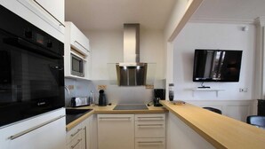 Una cucina compatta con forno Bosch, microonde e cappa aspirante in acciaio inossidabile. Presenta un piano di lavoro in legno e un piccolo lavandino.