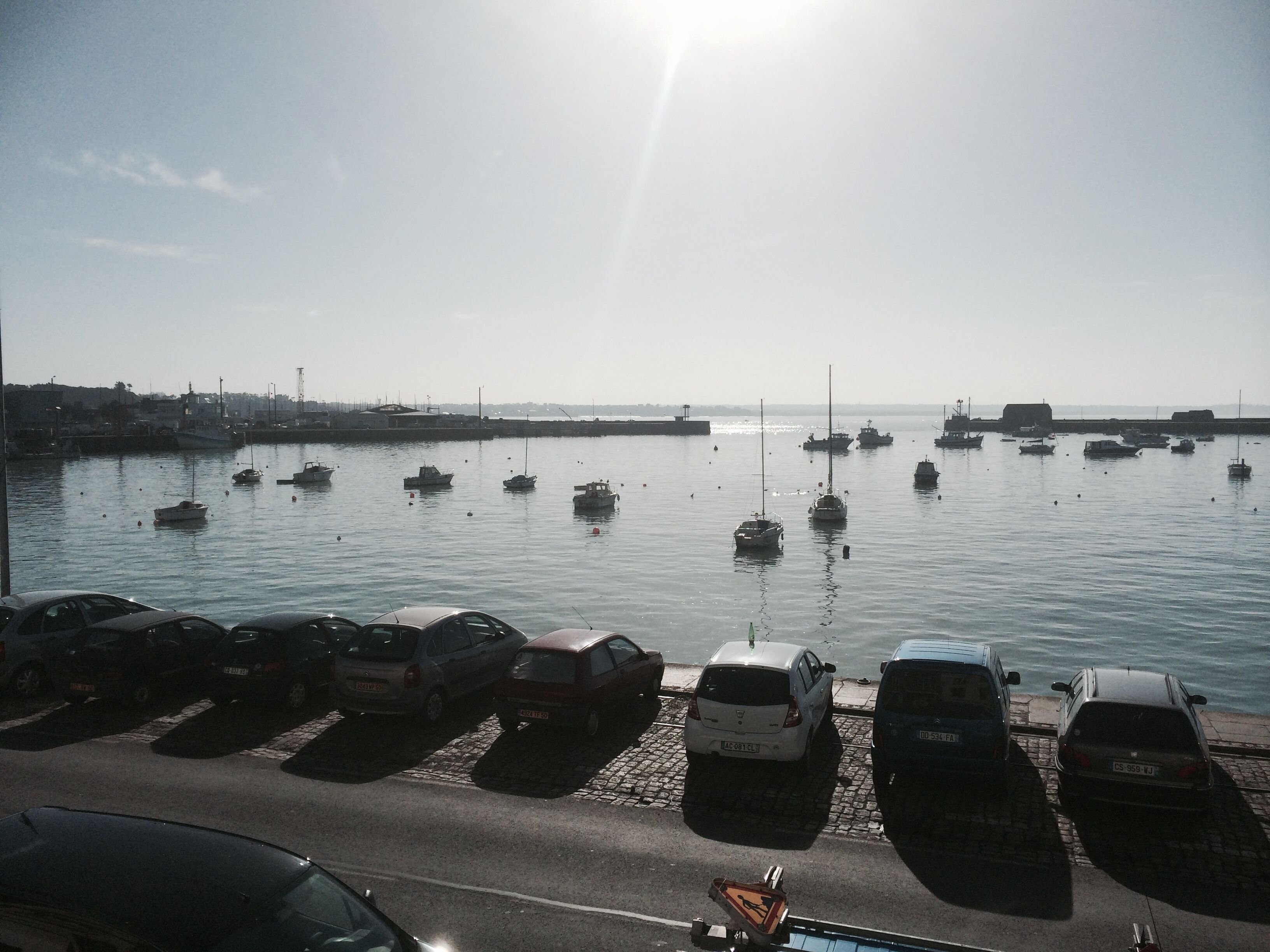 A marina with several boats docked, a parking area with cars, and a clear sky.