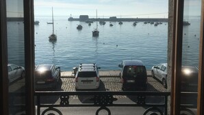 Vista dalla finestra su una marina con diverse imbarcazioni ormeggiate e auto parcheggiate lungo la riva.
