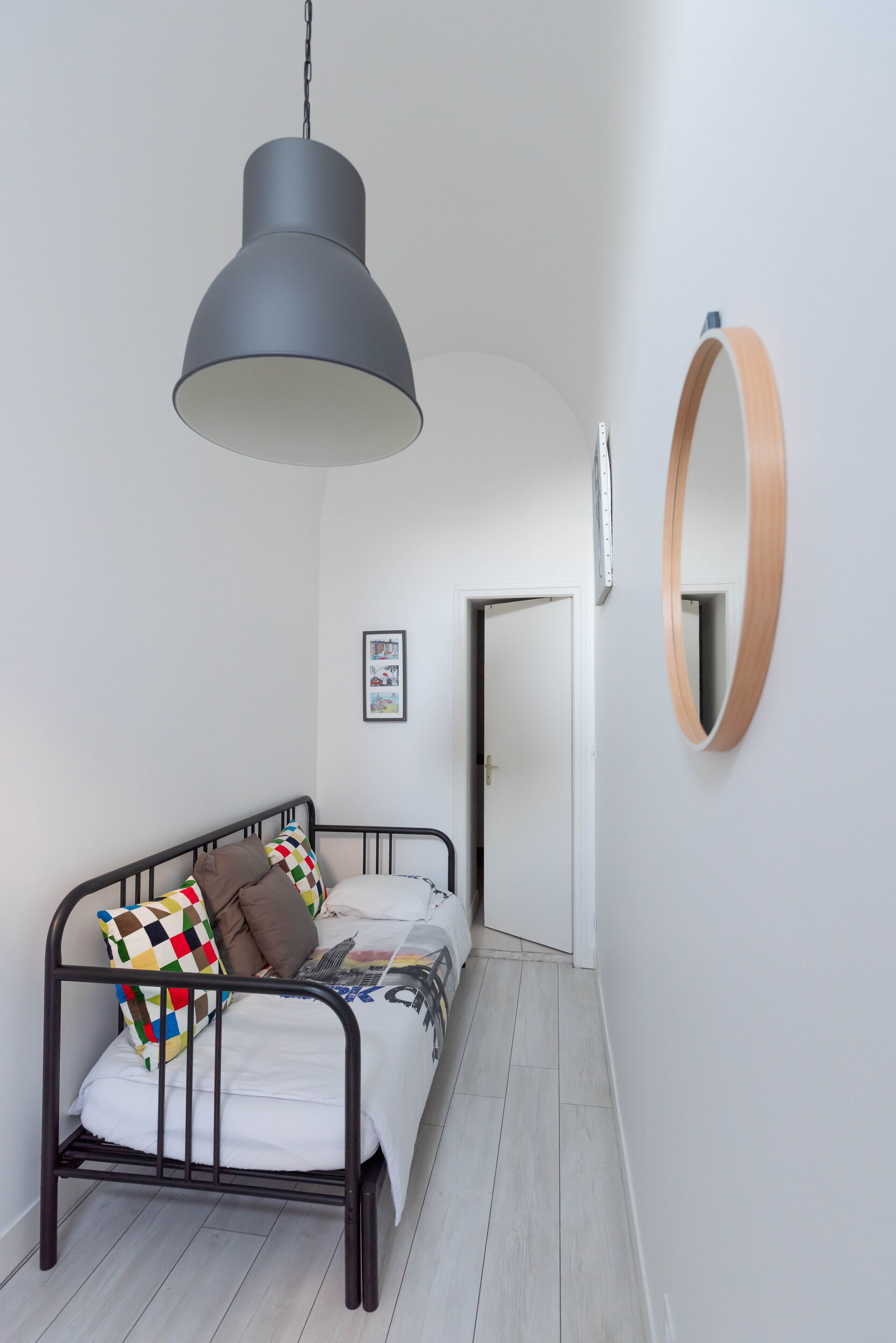 Une chambre à coucher avec un lit, un luminaire suspendu, un miroir encadré en bois et une porte donnant sur une autre pièce.