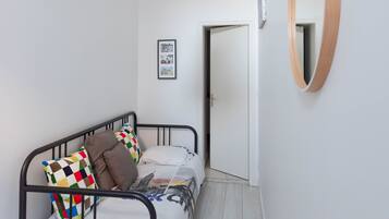 Une chambre à coucher avec un lit, un luminaire suspendu, un miroir encadré en bois et une porte donnant sur une autre pièce.
