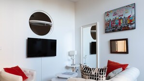 Una sala de estar moderna con un espejo redondo, un televisor de pantalla plana, una mesa redonda y dos sofás con cojines rojos.