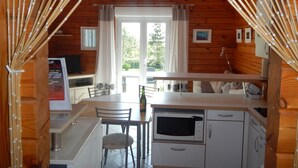 Interior de una cabaña de madera con una zona de cocina que incluye un microondas, una mesa de comedor con sillas y vistas por una ventana.