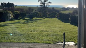 Vista desde una ventana sobre un campo cubierto de césped y una terraza de madera.