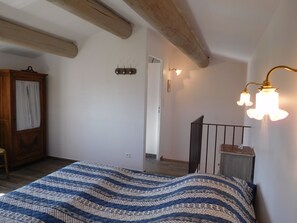 Ein Schlafzimmer mit Bett, Holzbalken, einem Kleiderschrank und einer Treppe.