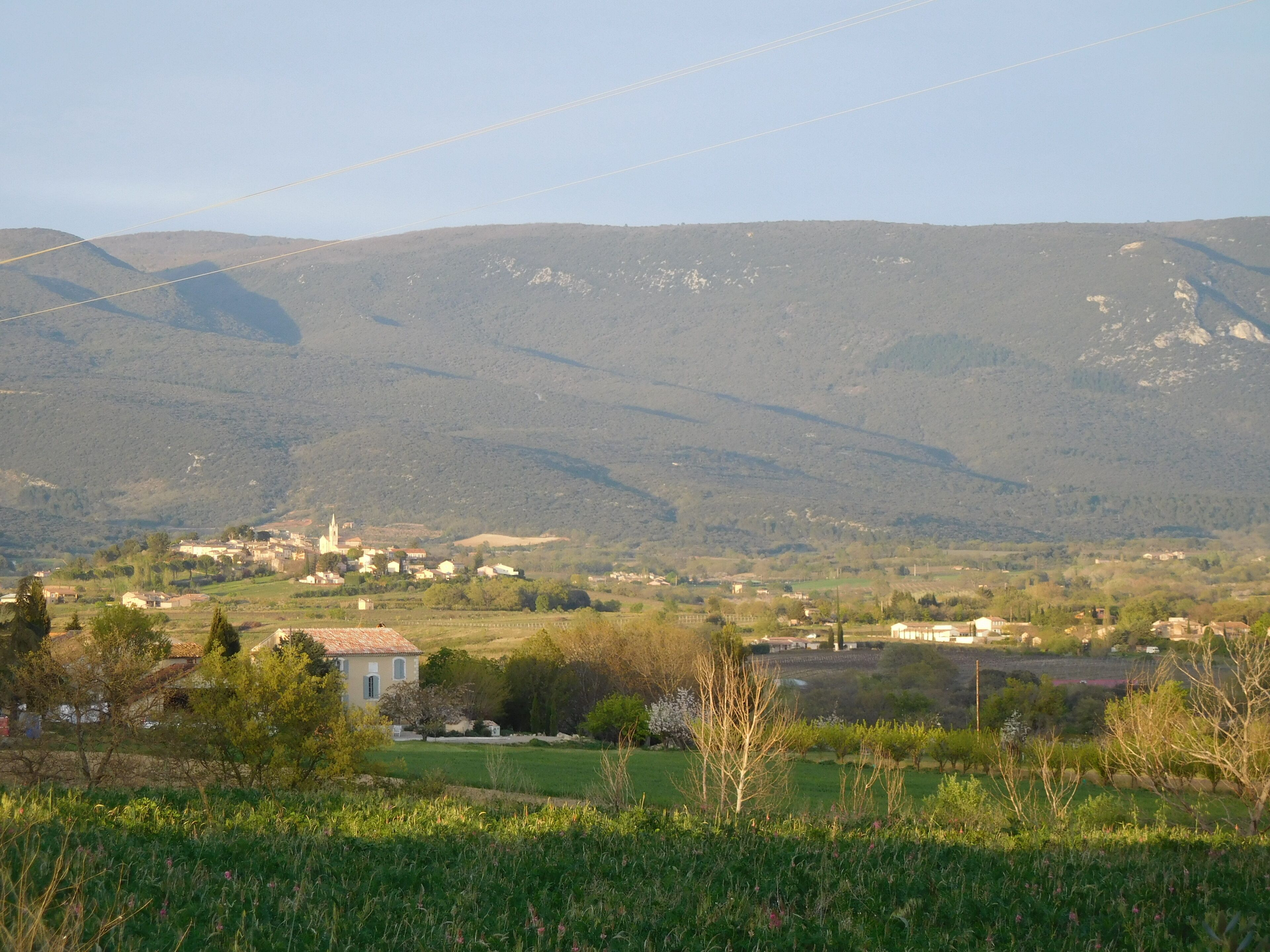 Un paysage rural avec un petit village, des champs verdoyants et des montagnes en arrière-plan.