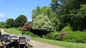 Un jardin avec une table et des chaises, entouré de verdure et d’arbres.