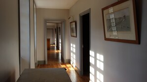 Un couloir au sol en bois, une porte sur la droite et un tableau encadré accroché au mur.