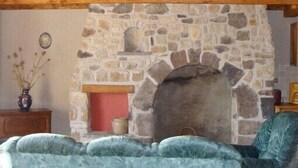 A stone fireplace with a wooden mantel, a rustic stone wall, and a cozy seating area with a plush blue sofa. - Old farmhouse tastefully renovated, very good comfort, (Ardes)