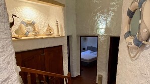 A narrow staircase with a wooden handrail, white textured walls, and a small shelf with nautical decorations.