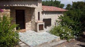 A rustic stone building with a tiled roof, a wooden door, and a small porch area.