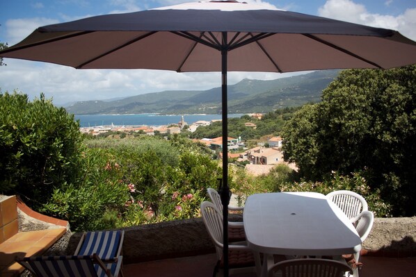 A terrace with a table and chairs, an umbrella, and a view of a coastal town and mountains. - Space, sun and freedom: 4 terraces, private garden, air-conditioned rooms.  (Propriano)
