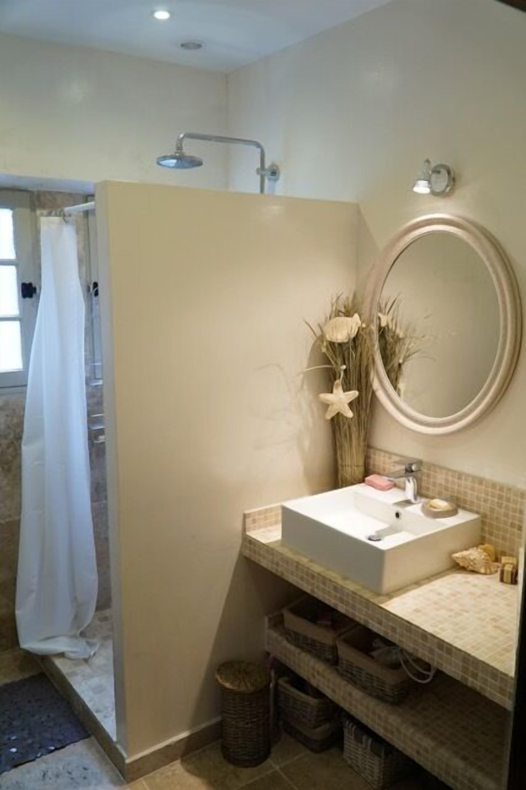 Une salle de bain équipée d’une douche, d’un lavabo, d’un miroir et de plantes décoratives.