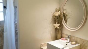 Une salle de bain équipée d’une douche, d’un lavabo, d’un miroir et de plantes décoratives.