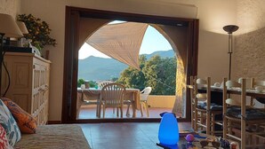 A room with a view of mountains, a dining area with chairs and a table, and a bed with pillows.