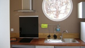 A compact kitchen with a built-in oven, a stainless steel sink, and a window with a view of trees. - T2 ground floor,  air conditioning placed in February 2023:)free public car park (Perpignan)