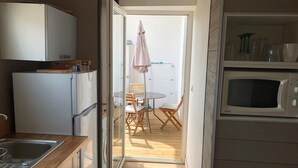 A compact kitchen with a refrigerator, microwave, and a small sink. There is a dining area with a table and chairs, and a sliding glass door leading to an outdoor space. - T2 ground floor,  air conditioning placed in February 2023:)free public car park (Perpignan)