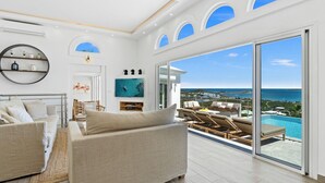 Ett rymligt vardagsrum med en stor soffa, en TV och utsikt över havet genom stora fönster.