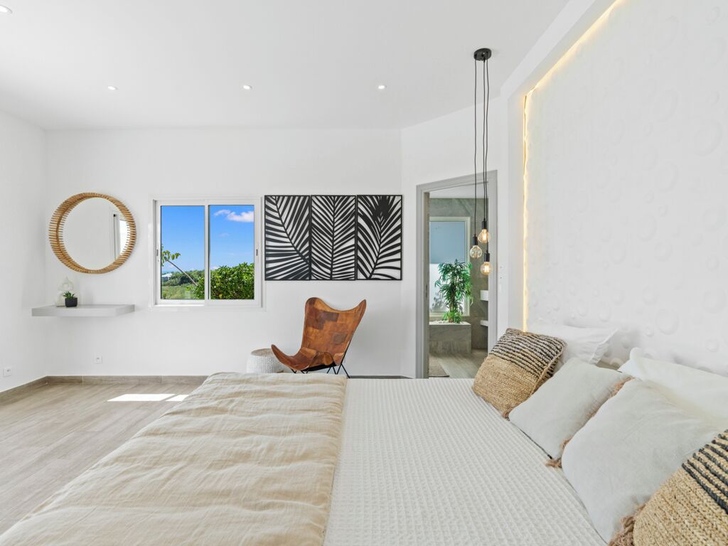 Une chambre à coucher moderne avec un grand lit, une chaise, un miroir et des œuvres d’art accrochées au mur.