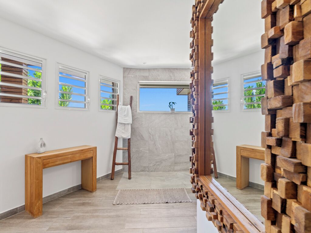 Une salle de bain avec un banc en bois, un porte-serviettes et une fenêtre donnant sur des palmiers.