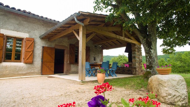Ein rustikales Steinhaus mit überdachter Terrasse, Außenbestuhlung und einem Steinkamin.