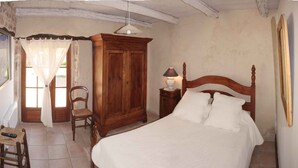 Ein Schlafzimmer mit einem hölzernen Bett, einem Nachttisch mit Lampe, einem Holzschrank, einem Stuhl und einem Fenster mit durchsichtigen Vorhängen.