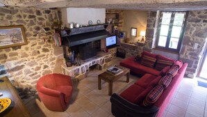 Ein gemütliches Wohnzimmer mit Kamin aus Stein, einer roten Couch, einem Holztisch und einem Fernseher.
