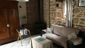 A cozy living room with a stone wall, a wooden door, a sofa, a small table, and a chair. - Country house heated pool 15 minutes from the Gulf of Morbihan (Sulniac)