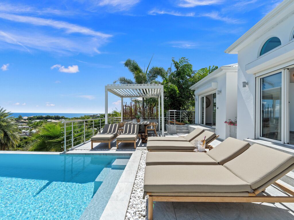 A poolside area with lounge chairs and a pergola, overlooking a scenic view.