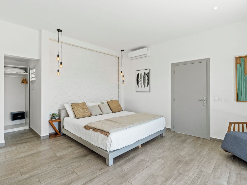 A modern bedroom with a large bed, a bedside table, a wardrobe, and a door.