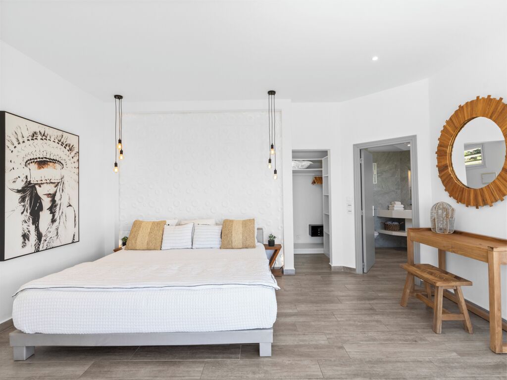 Een slaapkamer met een groot bed, een houten nachtkastje, een spiegel en een wandlamp.