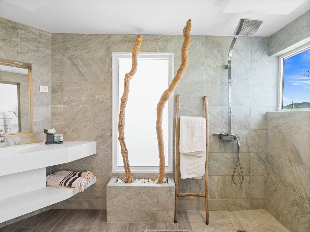 Un baño moderno con pared de mármol, tocador blanco, toallero de madera y ducha.