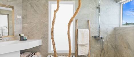 Un baño moderno con pared de mármol, tocador blanco, toallero de madera y ducha.