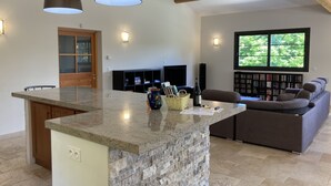 Una cocina amplia con una isla de granito, armarios de madera y horno empotrado. Hay un ventanal que ofrece vistas a zonas verdes.