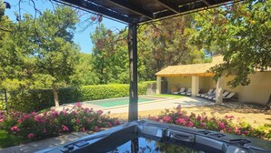 Un jacuzzi en un área exterior techada, con una piscina y sillones de descanso al fondo.