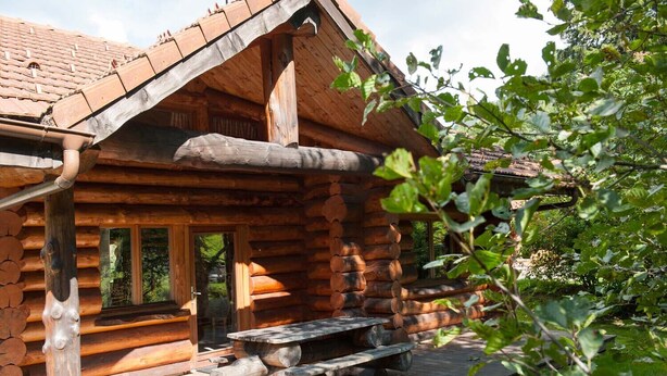 A log cabin with a wooden deck, a picnic table, and a door leading to the interior.
