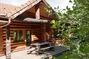 Une cabane en rondins avec une terrasse en bois, une table de pique-nique et une porte donnant sur l’intérieur.