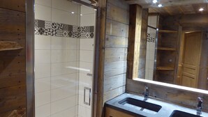 A wooden bathroom with a glass-enclosed shower, a large mirror, and a double sink vanity.