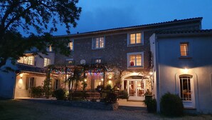 A building with multiple windows, a covered entrance with a bench, and outdoor lighting.