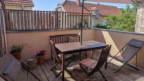 A wooden deck with a table and chairs, a potted plant, and a large umbrella providing shade. - Charming medieval house in the heart of Flavigny-sur-Ozerain (Flavigny-Sur-Ozerain)