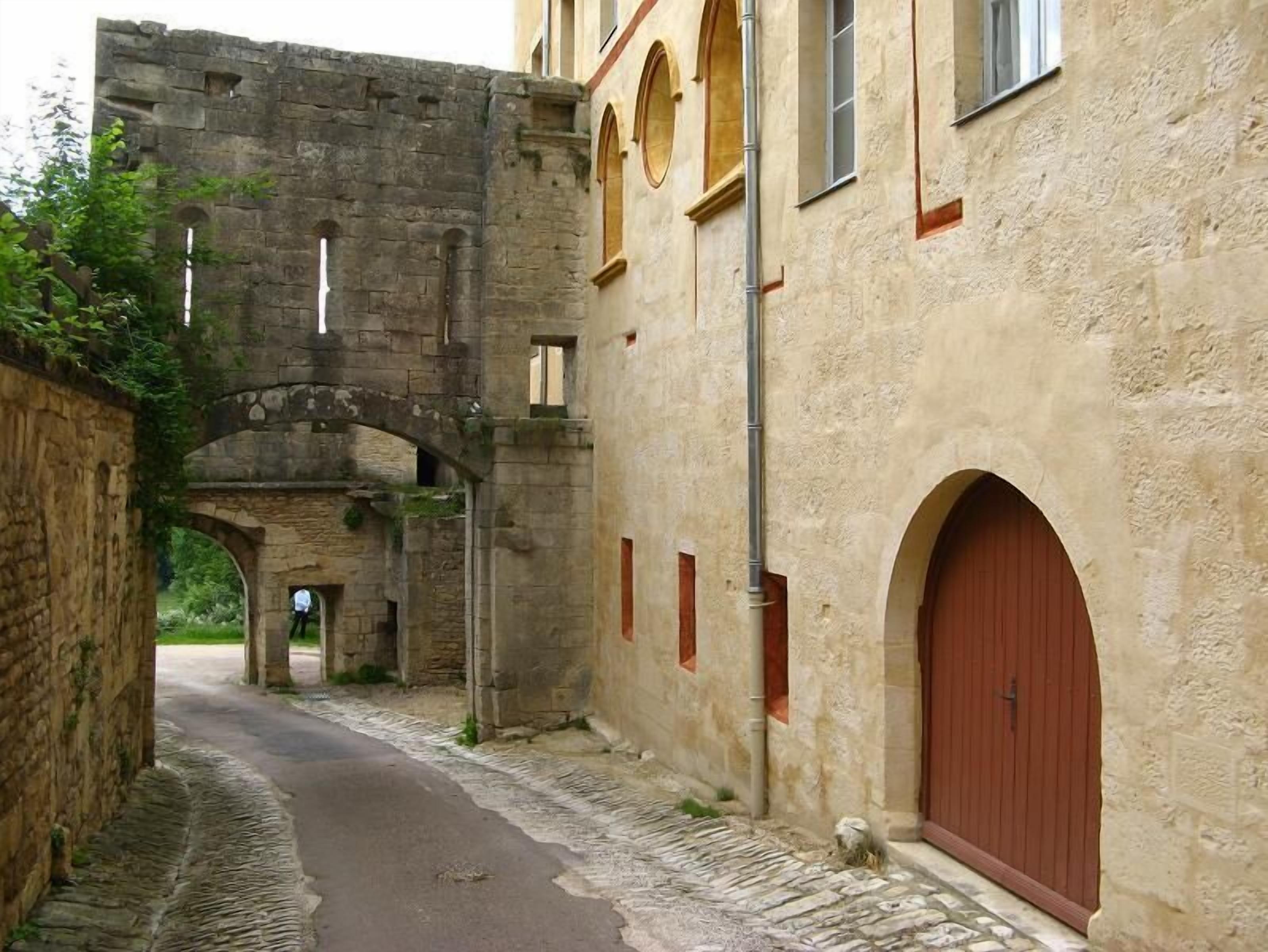 A narrow alleyway with a stone archway leading to a building with a red door and arched windows.