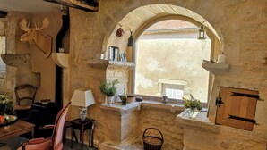 A rustic interior with stone walls, a fireplace, a wooden chair, a table, and a window with an arch. - Charming medieval house in the heart of Flavigny-sur-Ozerain (Flavigny-Sur-Ozerain)