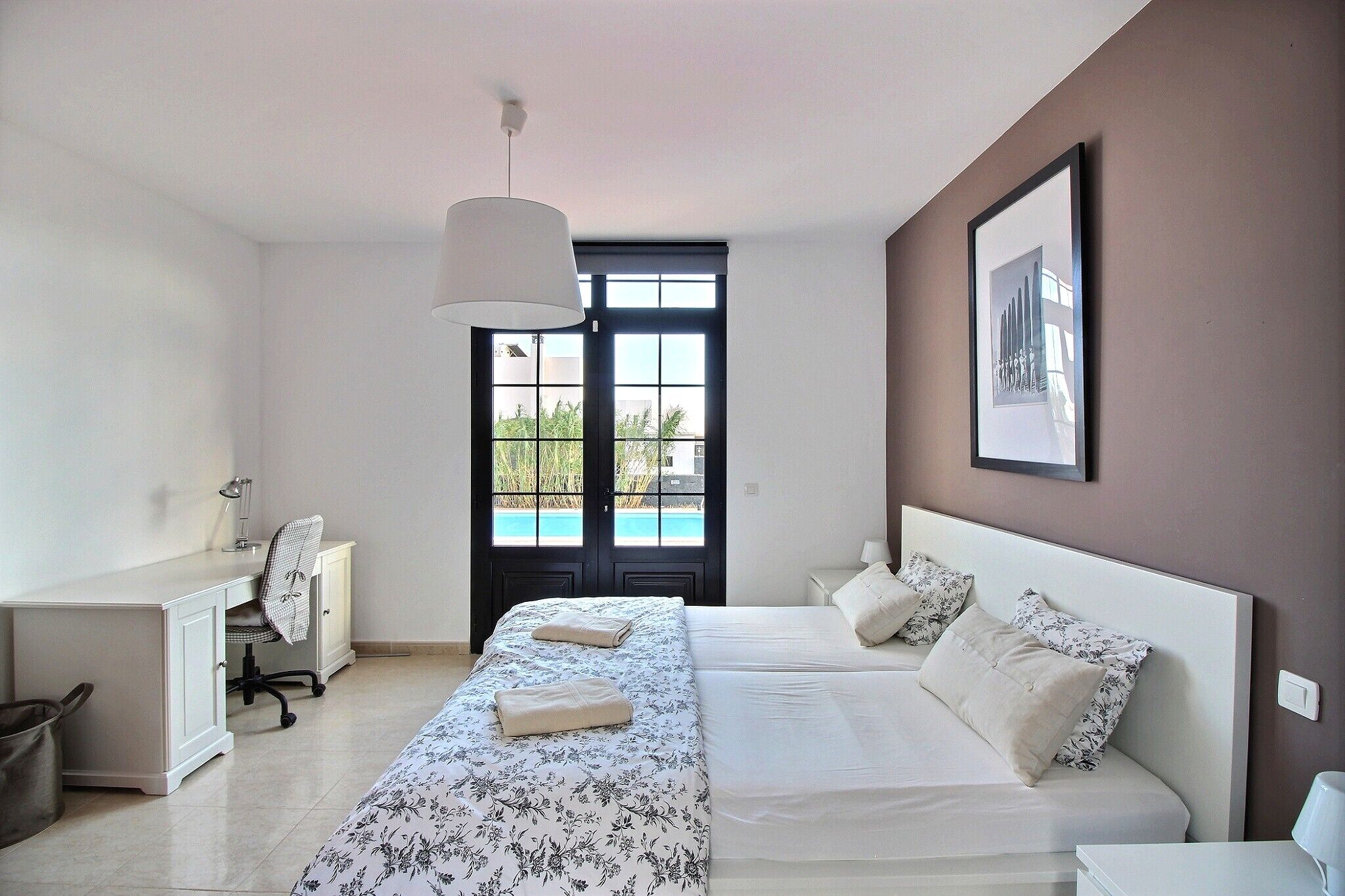 Une chambre avec un lit, un bureau et une chaise. Une porte donne accès à un balcon.