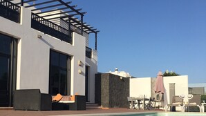 A modern pool area with a clear blue pool, a pergola with black railings, and outdoor seating with cushions. - Luxury villa with private heated pool, WIFI, views of the sea and volcanoes (TIAS)