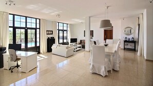 A spacious living area with a large window, a dining table with chairs, a sofa, and a TV. - Luxury villa with private heated pool, WIFI, views of the sea and volcanoes (TIAS)