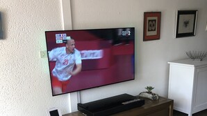 A television mounted on a wooden entertainment unit in a room with a white wall and a small white cabinet. - A cozy little nest in Biscarosse Lac, Superb high-end full option duplex (Biscarrosse)