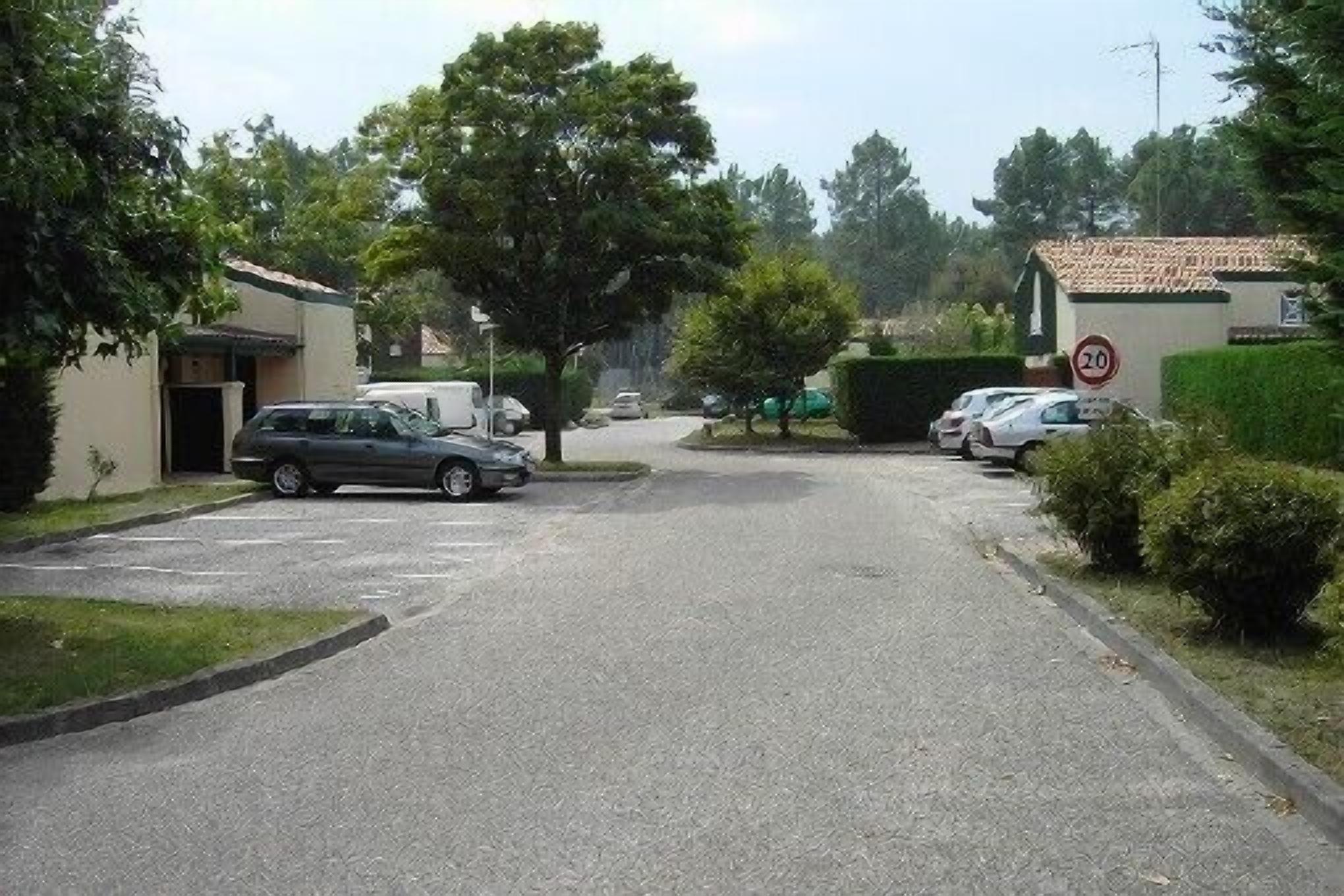 A residential street with parked cars, a speed limit sign, and houses with tiled roofs.