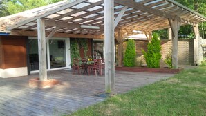 A covered patio with wooden flooring, a table with chairs, and a wooden pergola overhead.